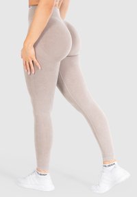 Beżowe legginsy z wysokim stanem, z akcentami w ribby, gładką fakturą i dopasowanym fasonem. Połączone z białymi butami sportowymi.