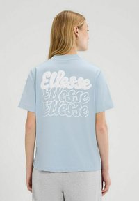 Lichtblauw t-shirt met korte mouwen, voorzien van grote witte letters op de achterkant, met een relaxte pasvorm en een gladde stoftextuur.