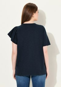 Granatowa koszulka z krótkimi bufkami, okrągłym dekoltem i luźnym krojem. Materiał wydaje się gładki z delikatnym połyskiem.