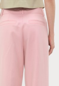 Gros plan de la vue arrière d'un pantalon large rose clair avec deux poches passepoilées, porté avec un haut beige.