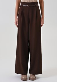 Braune Culotte-Hose mit Gürtel und Schnallendetail an der Taille, gefertigt aus strukturiertem Stoff, kombiniert mit einem gerippten Oberteil.