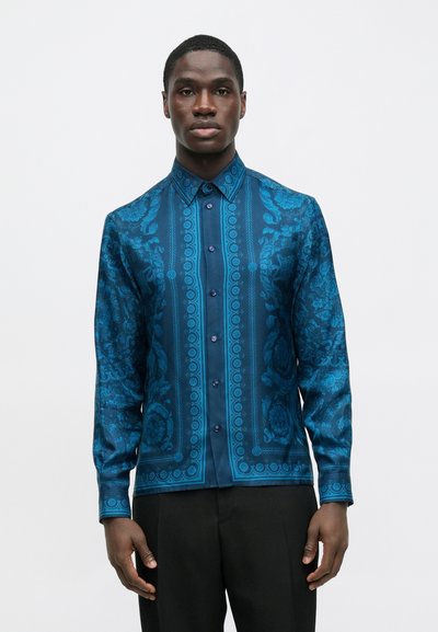 Hosszú ujjú, élénk kék szaténból készült ing, finom virágmintákkal és kontrasztos, egyszínű középső panellel. Gombos záródással és gallérral rendelkezik.