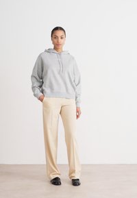 Hanorac gri din bumbac, cu glugă, cu o croială lejeră, asortat cu pantaloni bej, ajustați, și pantofi negri tip slip-on. Textură netedă, design minimalist.