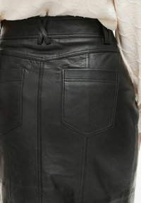 Musta nahkahame, jossa on tiukka leikkaus, näkyvät saumat, kaksi takataskua ja korkea vyötärö, jossa on hienovaraisia yksityiskohtia.