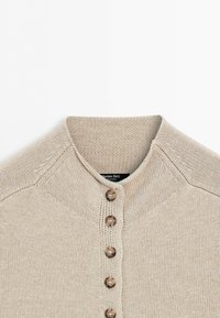 Beige knitted cardigan with five brown buttons and a round neckline, showing the upper front and collar area.
