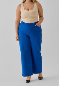 Modré kalhoty s širokými nohavicemi, bočními kapsami a hladkým materiálem, zkombinované s těsným tělovým topem. Design zahrnuje vysoký pas a volný střih.