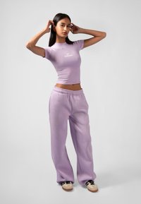 Fialový crop top s logom, spárovaný s voľnými teplákmi. Hladká textúra a elastický pás, skombinované so športovými teniskami.