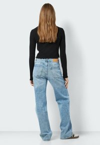 Šviesiai mėlyni tiesūs džinsai su aukštu juosmeniu, švelniu nudėvėjimu ir rudos odos etikete ant nugarinės juosmens dalies. Dėvima juoda prigludusi palaidinė.