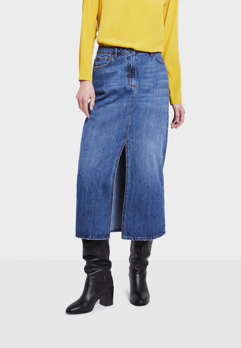 Denim midi suknja u plavoj boji s prednjim prorezom. Uparena s dugim žutim topom i crnim čizmama do koljena s potpeticom.