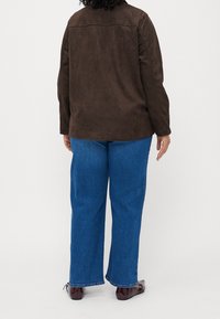 Hnědá semišová bunda s přímým střihem, spárovaná s modrými širokými džínami. Významné detaily zahrnují hladkou texturu a jednoduchý design.