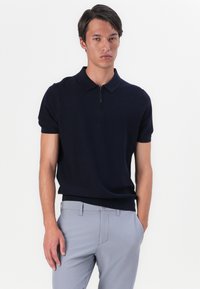 Mørk marineblå kortermet polo skjorte med glidelås krage, myk tekstur, tettsittende design, sammen med lysegrå tilpassede bukser.