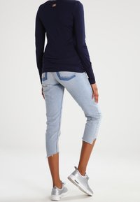 Marineblaues Langarmoberteil mit rundem Ausschnitt, kombiniert mit hellblauen, knöchellangen Jeans mit fransigen Säumen und silbernen Sneakers.