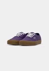 Lila kanvas sneakers med en strukturerad yta, vita snören och en tan gummisula. Har en märkt tagg på sidan. Klassisk låg toppdesign.