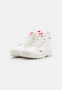 Baskets montantes blanches en toile texturée, avec des semelles en caoutchouc et des accents rouges sur la languette et l'étiquette latérale. Design à lacets.