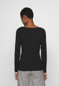 Czarny longsleeve z niskim, zaokrąglonym dekoltem. Materiał wydaje się gładki i dopasowany, w połączeniu z wzorzystymi spodniami w kratę.