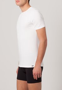 T-shirt bianco in cotone con maniche corte, design semplice, collo rotondo e un piccolo etichetta con logo all'orlo inferiore, abbinato a boxer neri.
