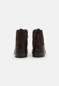 Botas de tobillo de cuero marrón con acentos de ante, que presentan una cremallera lateral, parte superior texturizada y suela robusta. La vista trasera muestra detalles de costura.