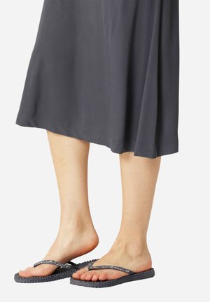 Black flip-flops with textured rubber soles and metallic glittery straps, paired with a flowing gray dress that reaches mid-calf.