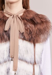 Faux pälskrage i brunt och vitt med ett beige tygband. Har en mjuk textur och dekorativa beslag i ändarna.