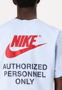 Osoba v světle modrém tričku Nike s červeným logem a textem "POUZE POVOLENÝ OSOBY" na zádech.