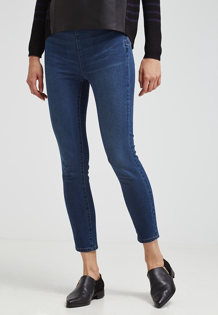 Jeans ajustados azul oscuro de mezclilla, con una textura suave, cintura media y corte hasta el tobillo, combinados con mocasines negros.