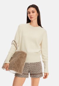 Cremefarbener Pullover mit gerippten Bündchen und Saum, kombiniert mit braunen strukturierten Shorts und einer flauschigen beigen Tasche mit einem gesteppten Muster.