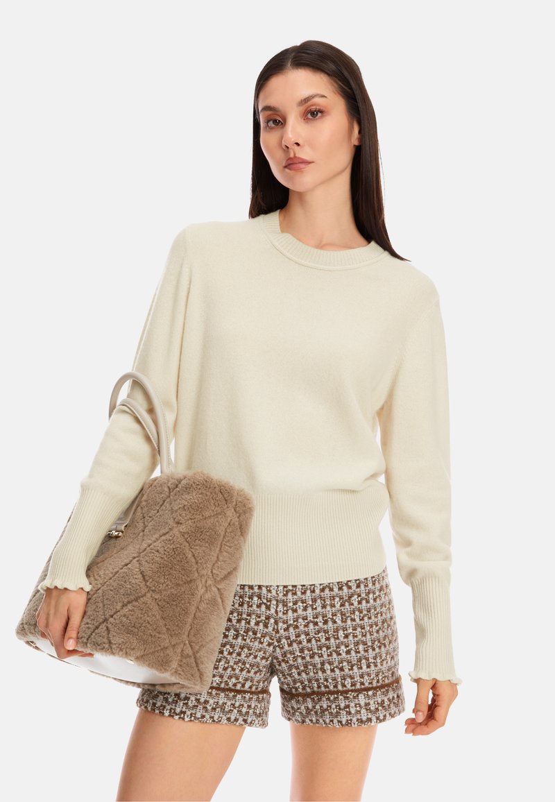 Cremefarbener Pullover mit gerippten Bündchen und Saum, kombiniert mit braunen strukturierten Shorts und einer flauschigen beigen Tasche mit einem gesteppten Muster.