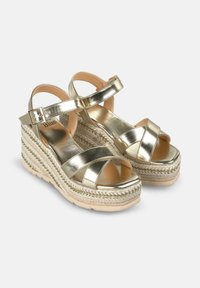 Metalen gouden wedge sandalen met een kruisbandontwerp, geweven touw middenzool en verstelbare enkelband. Glad oppervlak en platformbasis.