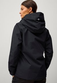 Giacca nera impermeabile con cappuccio, caratterizzata da un design elegante, una consistenza liscia e polsini regolabili. Logo discreto sul retro.