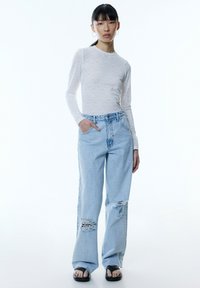 Langarm, lichtgrijs geribbeld topje; oversized lichtblauwe versleten jeans met scheuren; zwarte slip-on sandalen; minimalistisch ontwerp; losse pasvorm.
