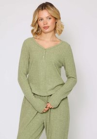 Langærmet, henley-style top i ribbet, lys grøn stof. Funktionen inkluderer en V-udskæring og placket med tre knapper. Blødt, tekstureret materiale.