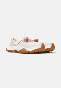 Zapatillas deportivas color blanquecino con suela de goma, que presentan una correa ancha en el empeine y un diseño suave y curvado.