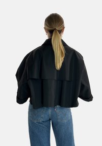 Giacca nera corta con una vestibilità rilassata, caratterizzata da un ampio collare e maniche lunghe. Indossata sopra jeans in denim a vita alta. Texture liscia.