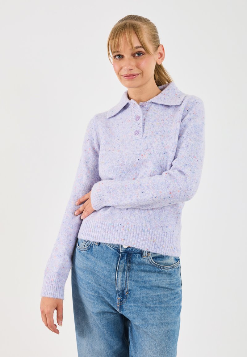 Maglione lavorato a maglia di un leggero viola con colletto, tre bottoni, polsini a coste e una texture chiazzata. Indossato con jeans in denim blu chiaro.