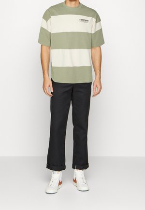 Olivengroen-wit gestreept T-shirt met een ronde hals en korte mouwen, gecombineerd met zwarte cropped broek en witte sneakers.