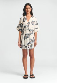 Květinové kimono šaty v béžové barvě s námořnickými a oranžovými akcenty. Obsahují široké rukávy, zavinovací design a odpovídající pásek. Hladká textura.