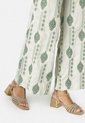 Pantaloni crema a gamba lunga con motivi di foglie verdi abbinati a sandali beige con cinturini e tacco a blocco, decorati con piccoli strass.