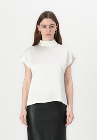 Haut blanc à manches courtes avec un col montant en tissu lisse et léger. Associé à une jupe en cuir noir ajustée.
