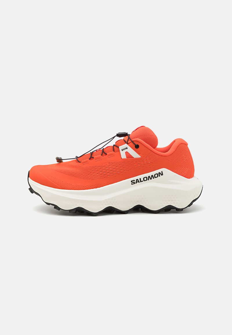 Oranje trailrunning schoenen met bovenkant van gaas, witte tussenzool, textuuroverlays in zwart op de zool en verstelbare bungee veters. Merken op de zijkant.