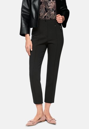 Black tailored pants with a slim fit, featuring zip and button closure, and side pockets. Paired with light pink ballet flats.
