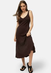 Maxi dress marrone scuro con un motivo testurizzato, scollo a V e spalline sottili. Abbinato a ciabatte nere per un look casual.