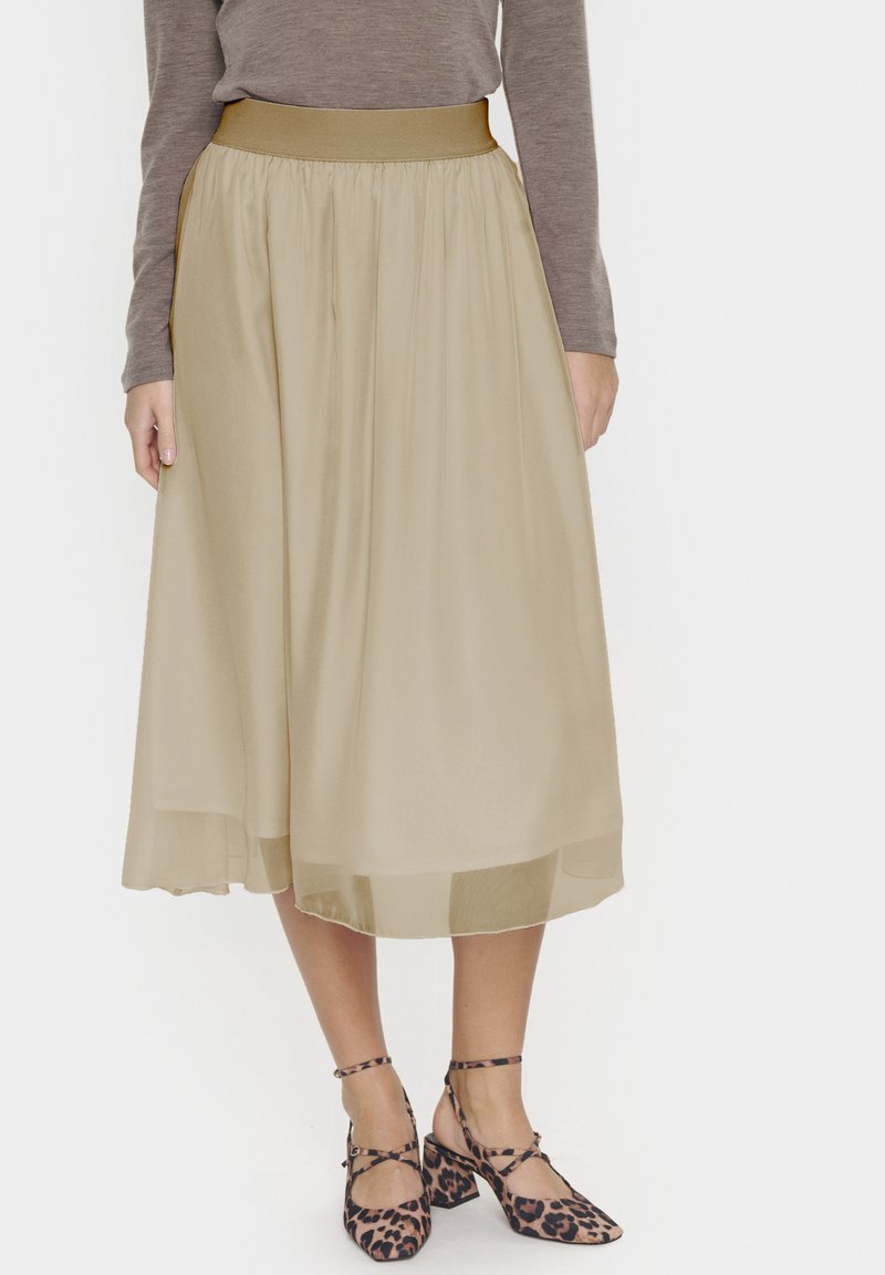 Jupe beige longueur genou en tissu léger avec une taille froncée et une doublure intérieure lisse ; portée avec des chaussures à talons carrés imprimé léopard.