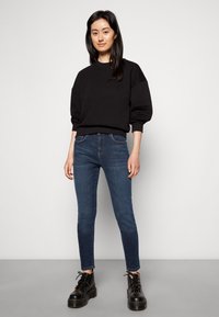 Sweatshirt preto com mangas oversized, combinado com jeans skinny azul escuro e botas pretas de plataforma com atacadores. Design simples e funcional.