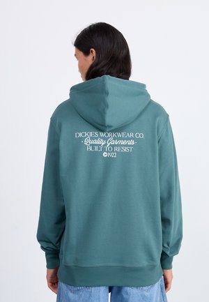 Teal hoodie met een ruime capuchon, ribgebreide manchetten en zoom. De achterkant heeft witte tekst: "DICKIES WORKWEAR CO. Kwaliteitskleding. GEBUIGD OM TE WEERSTAAN ©1922".