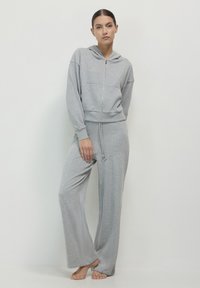 Ensemble de salon gris composé d'un sweat à capuche zippé avec une poche avant et de pantalons à jambes larges, fabriqué dans un tissu doux avec une texture lisse.