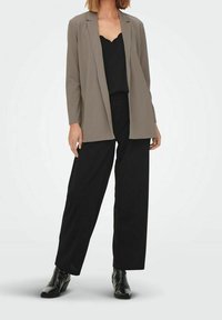 Lichtgrijze blazer over een zwarte scalloped tanktop, gecombineerd met zwarte wijde broek en zwarte enkellaarsjes. Gladde texturen doorheen.