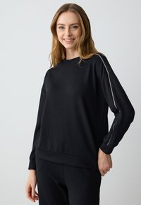 Black sweatshirt with long sleeves, round neckline, and subtle silver accent along the sleeves. Soft, smooth fabric with relaxed fit.