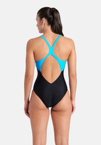 One-piece swimsuit with a blue top and black bottom. Crossback design with an open back and smooth, stretchy fabric texture.