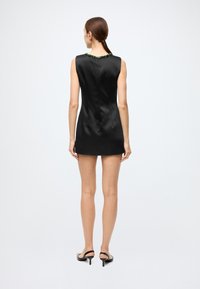 Black sleeveless mini dress with a smooth satin texture, features a green beaded accent along the neckline. Simple and fitted design.