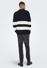 Suéter de punto trenzado en navy con rayas horizontales blancas, cuello redondo, patrón texturizado y puños de canalé, combinado con jeans oscuros y botas negras.